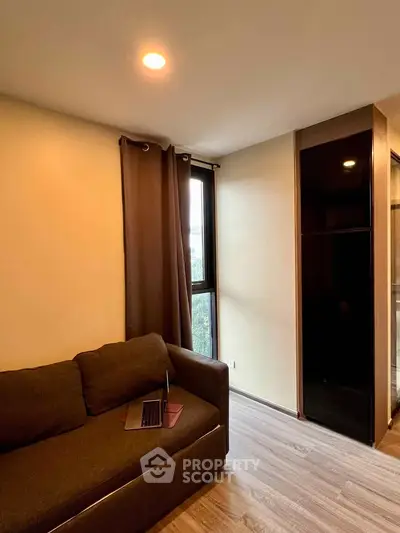 Cozy living room with brown sofa and natural light from large window, ideal for relaxation.