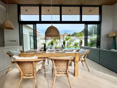 Luxurious open-plan living room with pool view, featuring elegant wicker furniture and floor-to-ceiling windows.