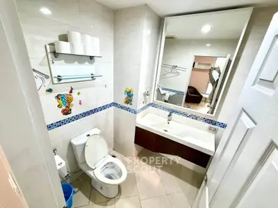 Modern bathroom with large mirror and decorative tiles, featuring a sleek sink and toilet.