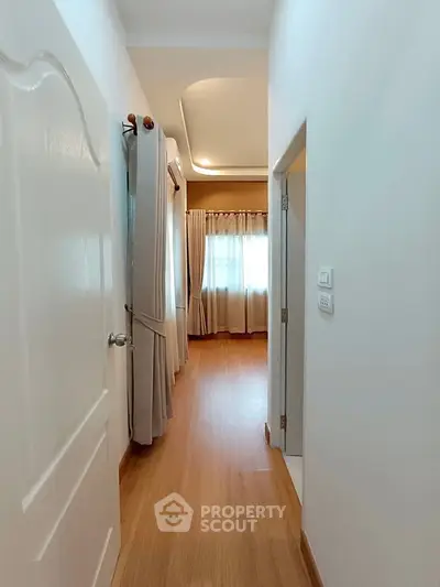 Bright hallway leading to a cozy bedroom with wooden flooring and elegant curtains.