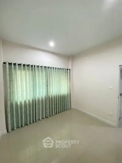 Spacious empty room with tiled floor and large window with curtains