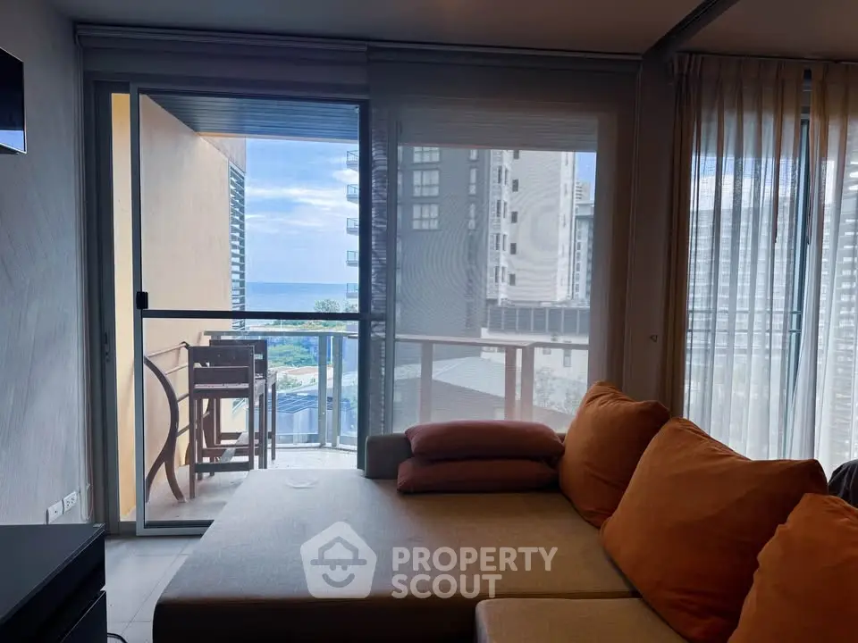 Modern living room with cozy sofa and balcony offering stunning ocean view in urban high-rise apartment.