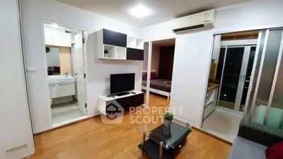 Modern apartment interior with open living room and bedroom, featuring sleek furniture and wooden flooring.