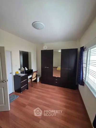 Spacious bedroom with wooden flooring, large wardrobe, and study desk, perfect for comfortable living.