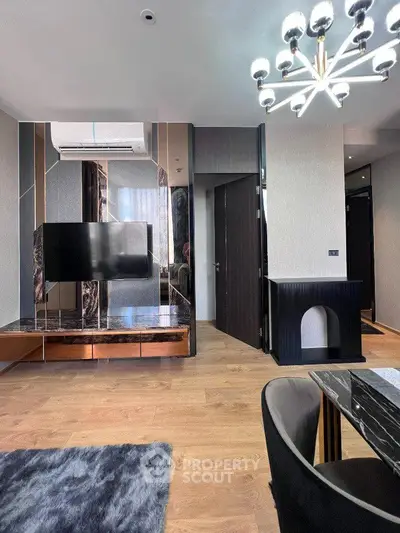 Modern living room with stylish decor, featuring a sleek TV unit, elegant chandelier, and plush rug.