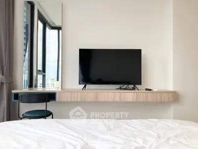 Modern bedroom with wall-mounted TV and large window offering natural light.