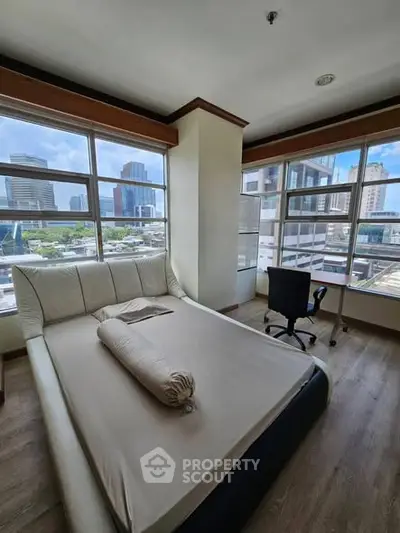 Modern bedroom with city view, featuring a cozy bed and workspace in a high-rise apartment.