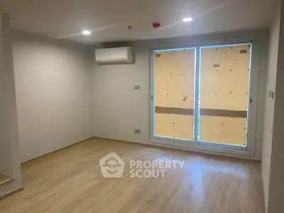 Spacious unfurnished room with wooden flooring and large window, ideal for customization.