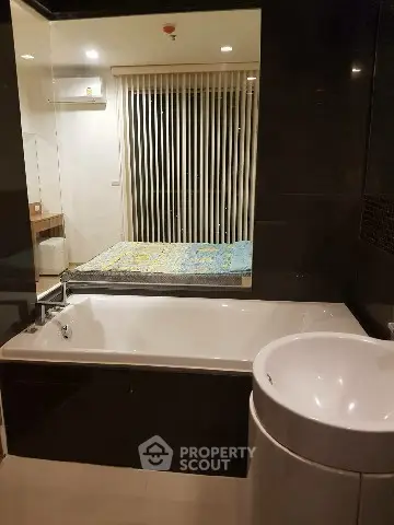 Modern bathroom with bathtub and view into adjacent bedroom through glass wall.