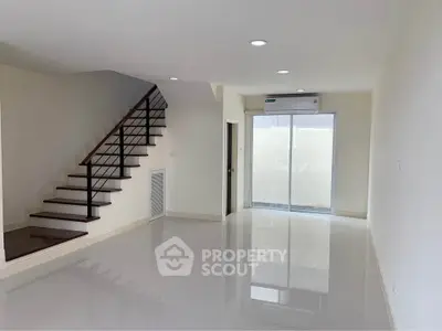 Spacious modern living room with sleek staircase and large windows for natural light.
