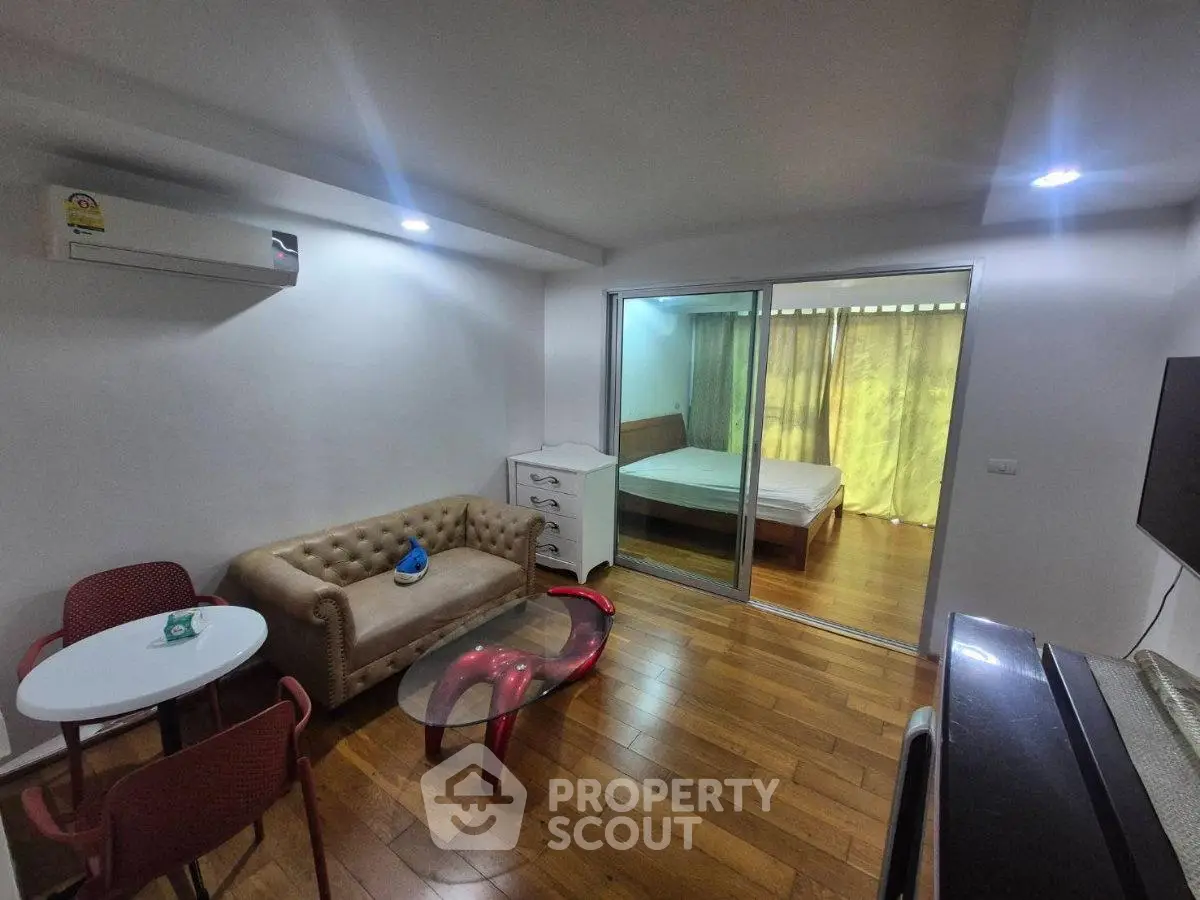 Modern living room with wooden flooring, cozy sofa, and sliding glass doors leading to a bedroom.