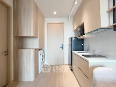Modern kitchen with sleek cabinetry, washing machine, and black fridge in a compact open layout.