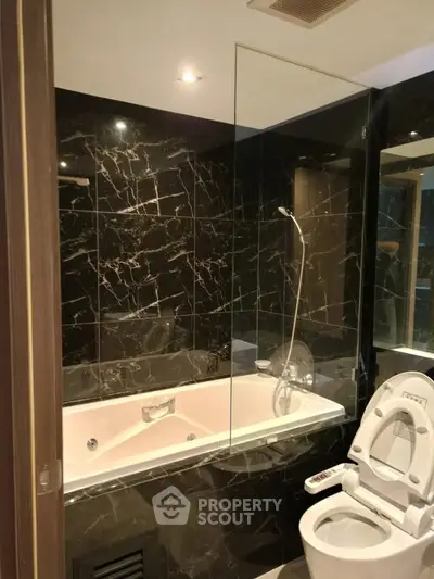 Luxurious bathroom with marble walls and modern fixtures, featuring a sleek bathtub and high-tech toilet.