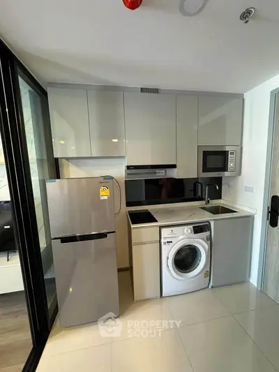 Modern compact kitchen with sleek appliances and washing machine in stylish apartment.