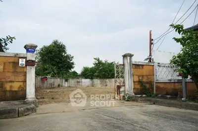 Vacant land with gated entrance and surrounding greenery, ideal for development.