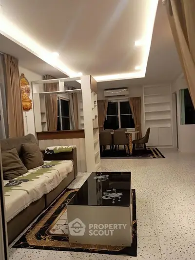 Spacious living room with modern decor and dining area, featuring elegant lighting and large windows.