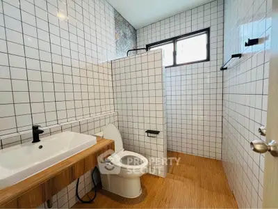 Modern bathroom with white tiles and wooden accents, featuring a sleek sink and toilet.