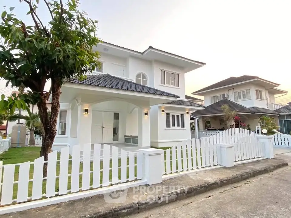 Charming two-story white house with picket fence and lush green lawn in a serene neighborhood.