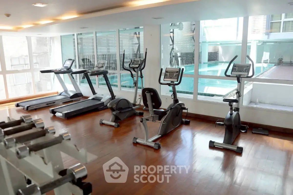 Modern gym with exercise equipment and pool view in luxury apartment complex.