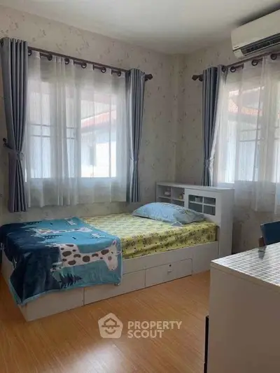 Cozy bedroom with natural light, featuring a single bed, wooden flooring, and air conditioning.