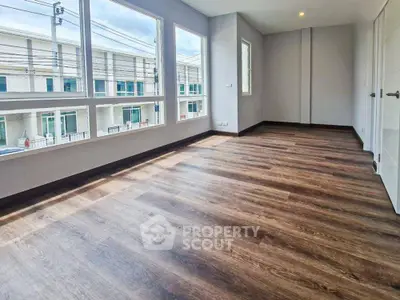 Spacious empty room with large windows and wooden flooring in modern townhouse.