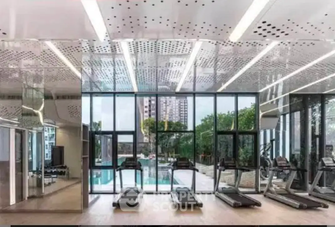 Modern gym with floor-to-ceiling windows overlooking a pool and lush greenery.
