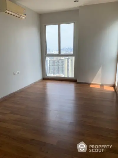 Spacious empty room with wooden flooring and city view from window