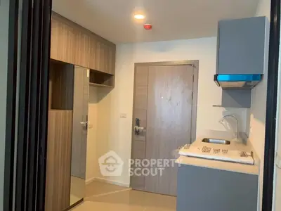 Modern apartment entrance with compact kitchen and sleek cabinetry.