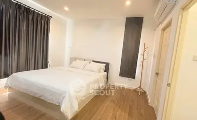 Spacious bedroom with modern decor and wooden flooring, featuring a comfortable bed and ample natural light.