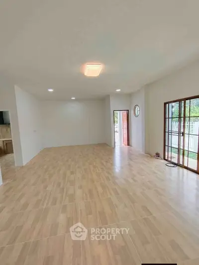 Spacious open-plan living room with wooden flooring and large windows for natural light.