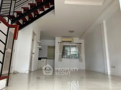 Spacious open-plan living area with staircase and tiled flooring, featuring a compact kitchen and air conditioning.