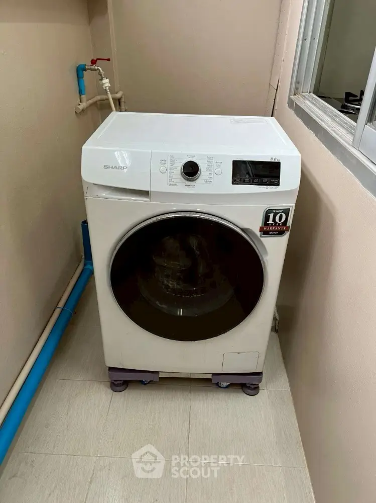 Modern washing machine in a compact laundry area with beige walls and tiled floor.