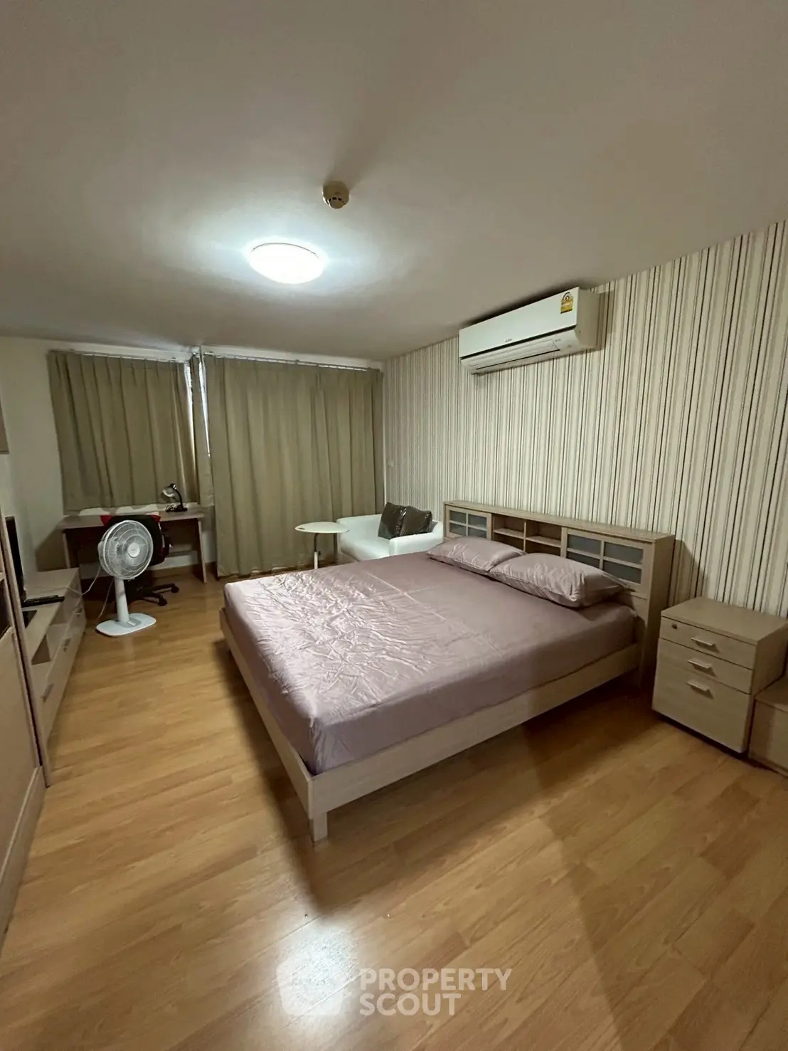 Spacious bedroom with modern furnishings and wooden flooring, featuring a cozy ambiance.