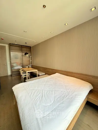 Modern bedroom with wooden furniture and dining area, featuring a cozy bed and stylish lighting.
