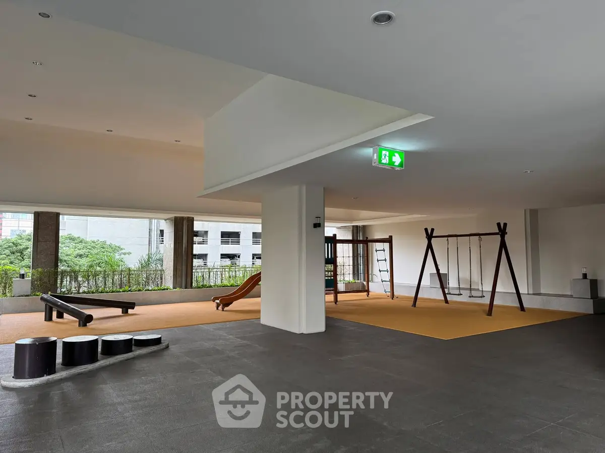 Spacious indoor playground area in modern residential building with swings and slide.