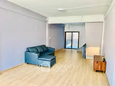 Spacious living room with modern sofa and wooden flooring, featuring ample natural light and minimalist decor.
