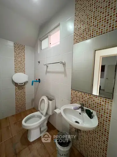 Modern bathroom with tiled walls and wooden floor, featuring a toilet and sink.