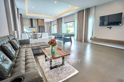 Spacious modern living room with leather sofa, pool table, and open kitchen layout.