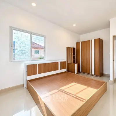 Spacious bedroom with modern wooden furniture and large window offering natural light.