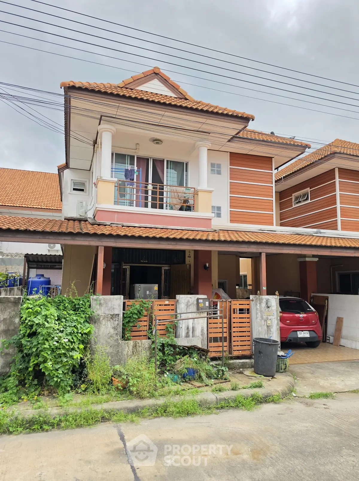 Charming two-story house with a red-tiled roof and balcony in a suburban neighborhood.