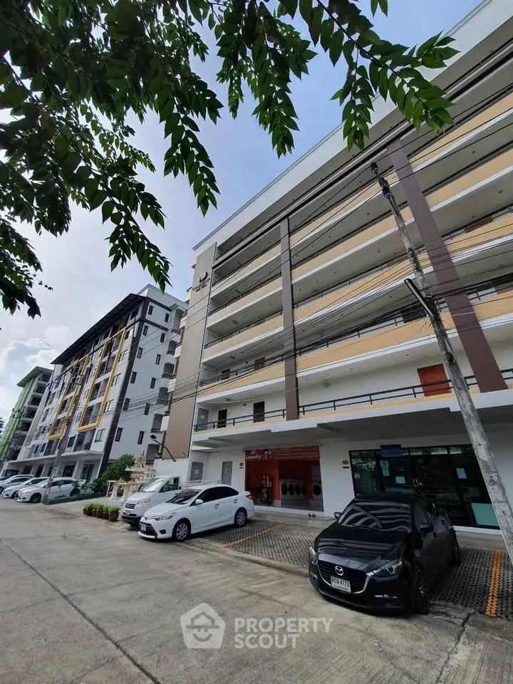 Modern multi-story apartment building with parking area and lush greenery.