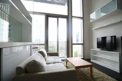 Modern living room with high ceilings and large windows offering city views.