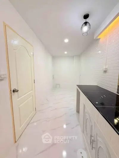 Sleek modern kitchen with white cabinetry and black countertop, featuring elegant lighting and spacious design.