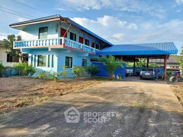 Charming two-story blue house with spacious driveway and carport, surrounded by lush greenery.