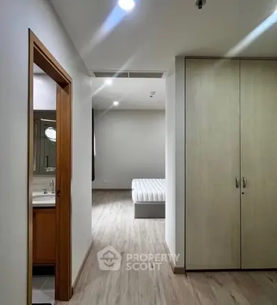Modern apartment hallway leading to a cozy bedroom with wooden flooring and built-in wardrobe.