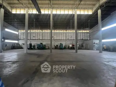 Spacious industrial warehouse with high ceilings and machinery, ideal for manufacturing or storage.