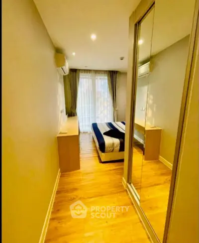Cozy bedroom with mirrored wardrobe and wooden flooring, featuring natural light and modern decor.