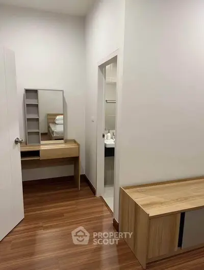 Modern bedroom with wooden flooring and vanity desk, adjacent to a compact bathroom.