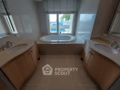 Luxurious bathroom with dual sinks and a central bathtub, offering a serene view through the window.