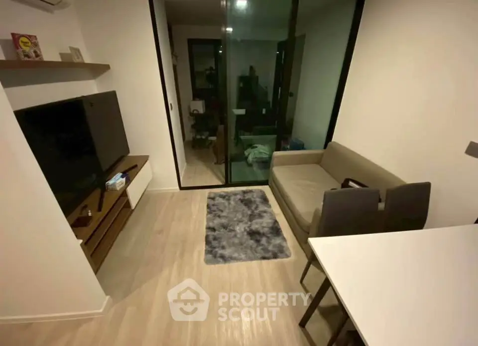 Modern living room with sleek furniture and glass door leading to a cozy balcony.